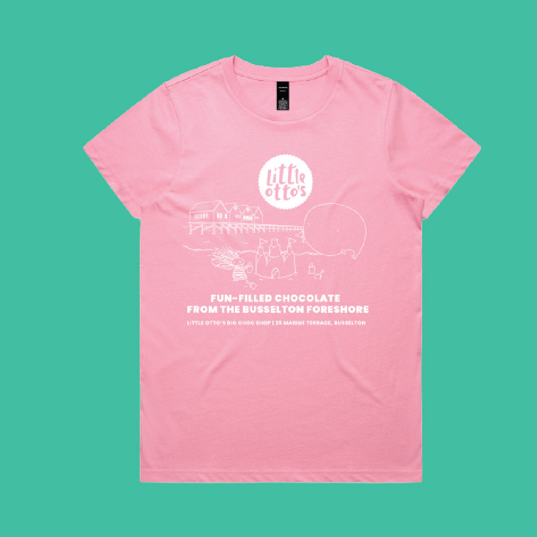 A light pink short-sleeve t-shirt with a white graphic print on the front, featuring the text 'little otes' and 'FUN-FILLED CHOCOLATE FROM THE BUSELTON FORESHORE', displayed flat against a solid teal background.