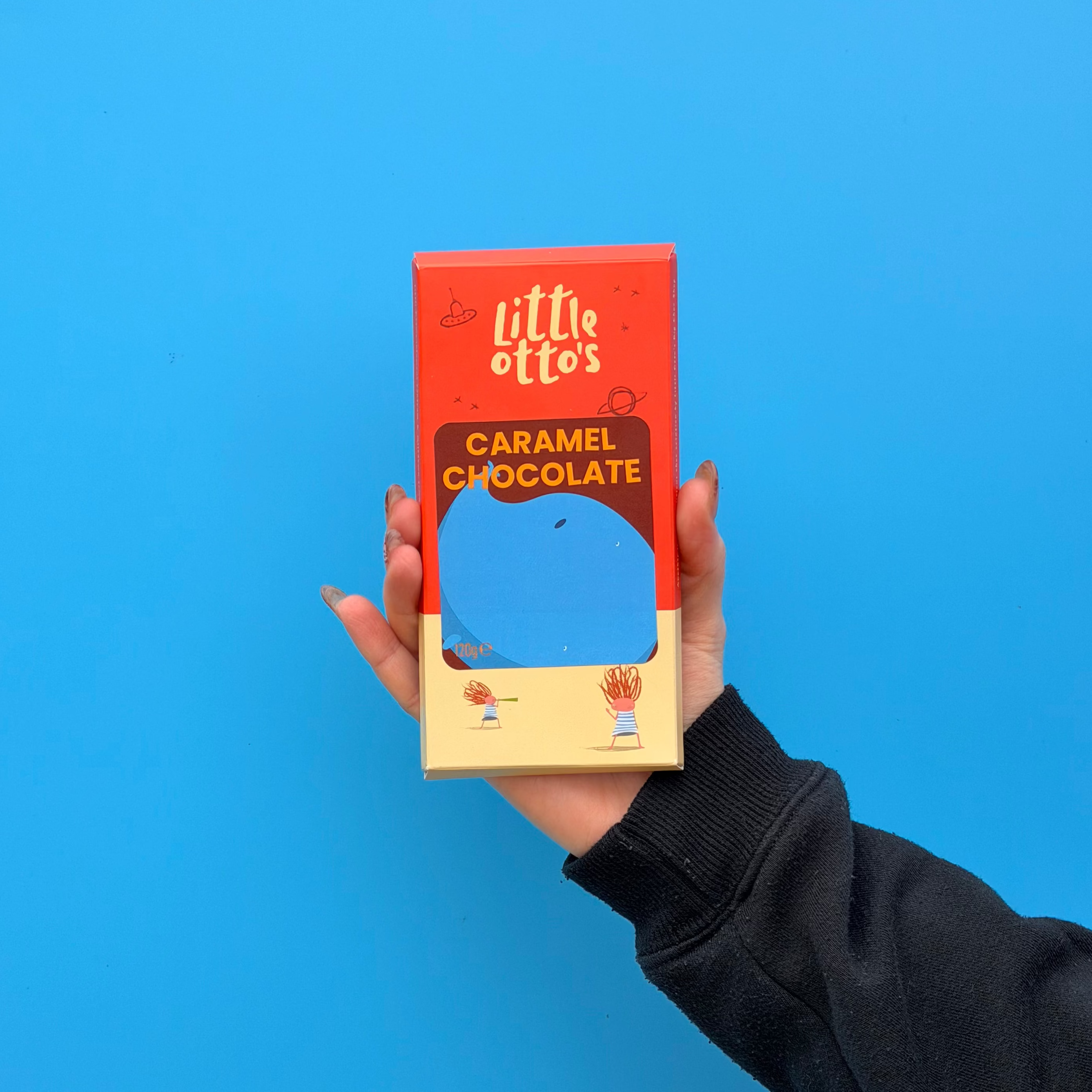 Little Otto's worker holding caramel chocolate bar in front of blue wall in Busselton