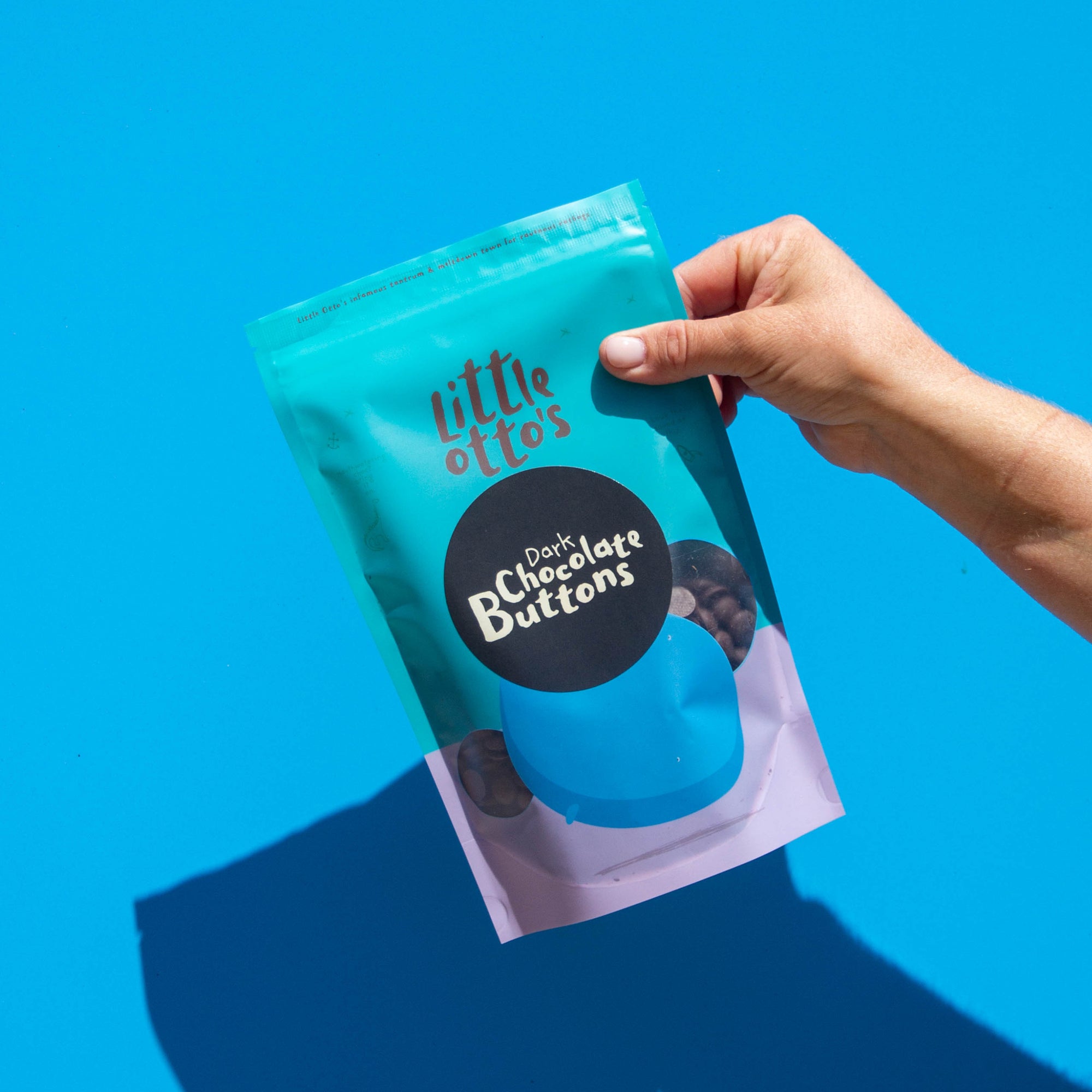 Little Otto's Staff holding Dark Chocolate Buttons 250g Infront of Busselton blue wall