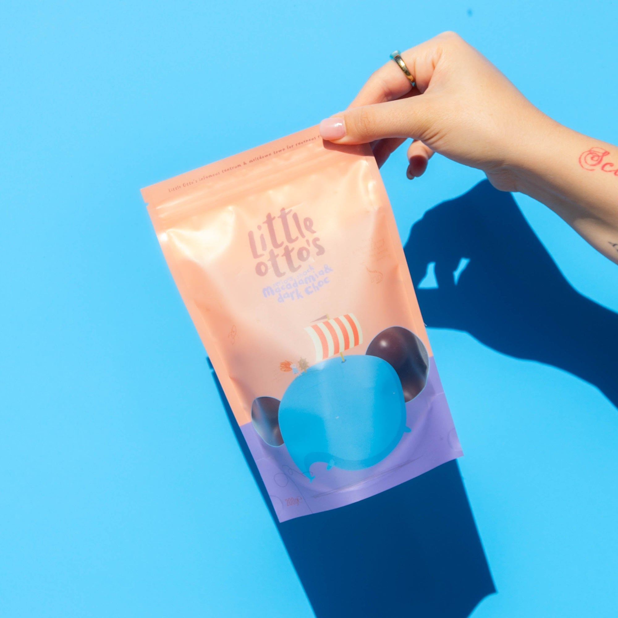 Little Otto's Staff holding Dark Chocolate and Macadamia 200g Infront of Busselton blue wall