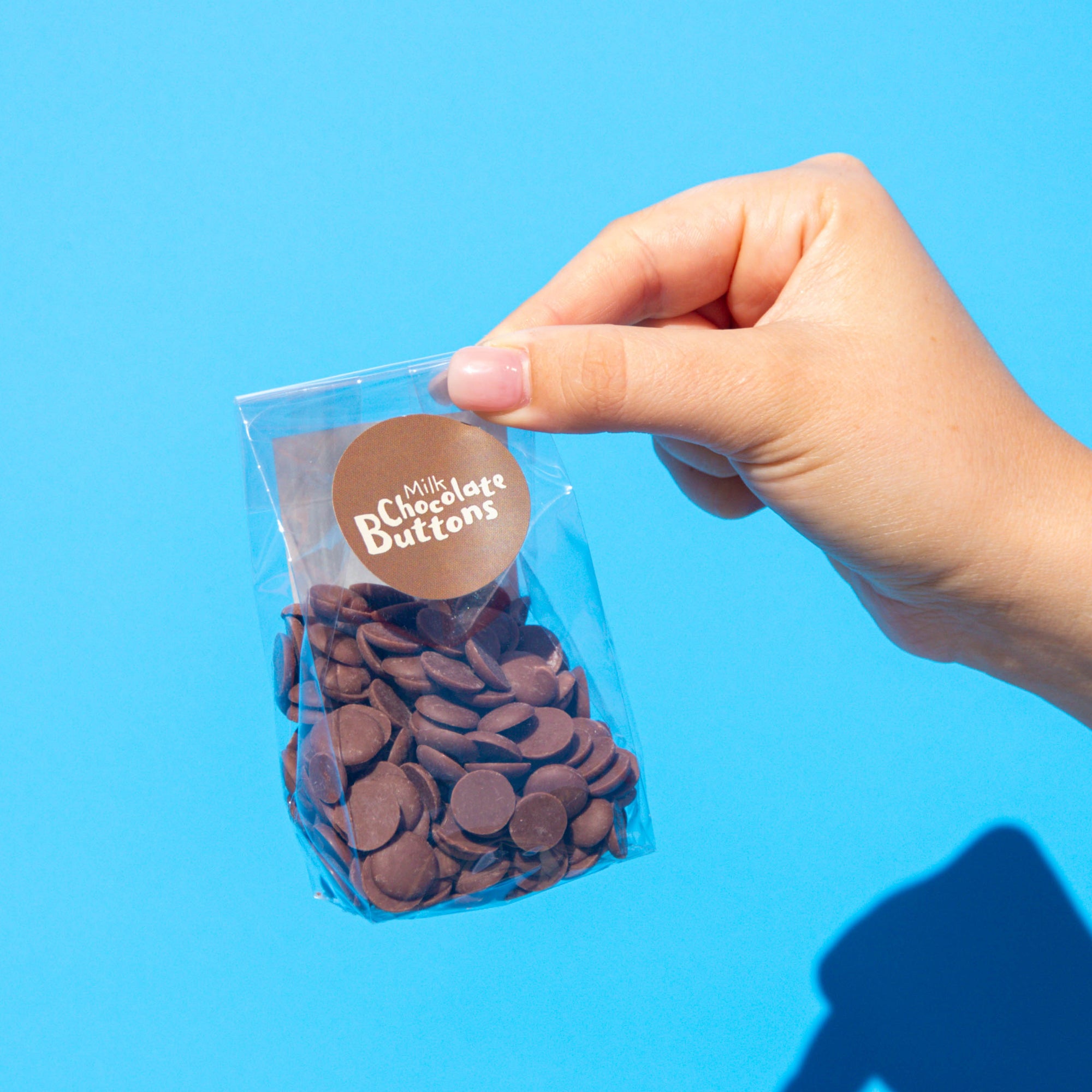 Little Otto's Staff Milk Chocolate Buttons 100g holding Infront of Busselton blue wall