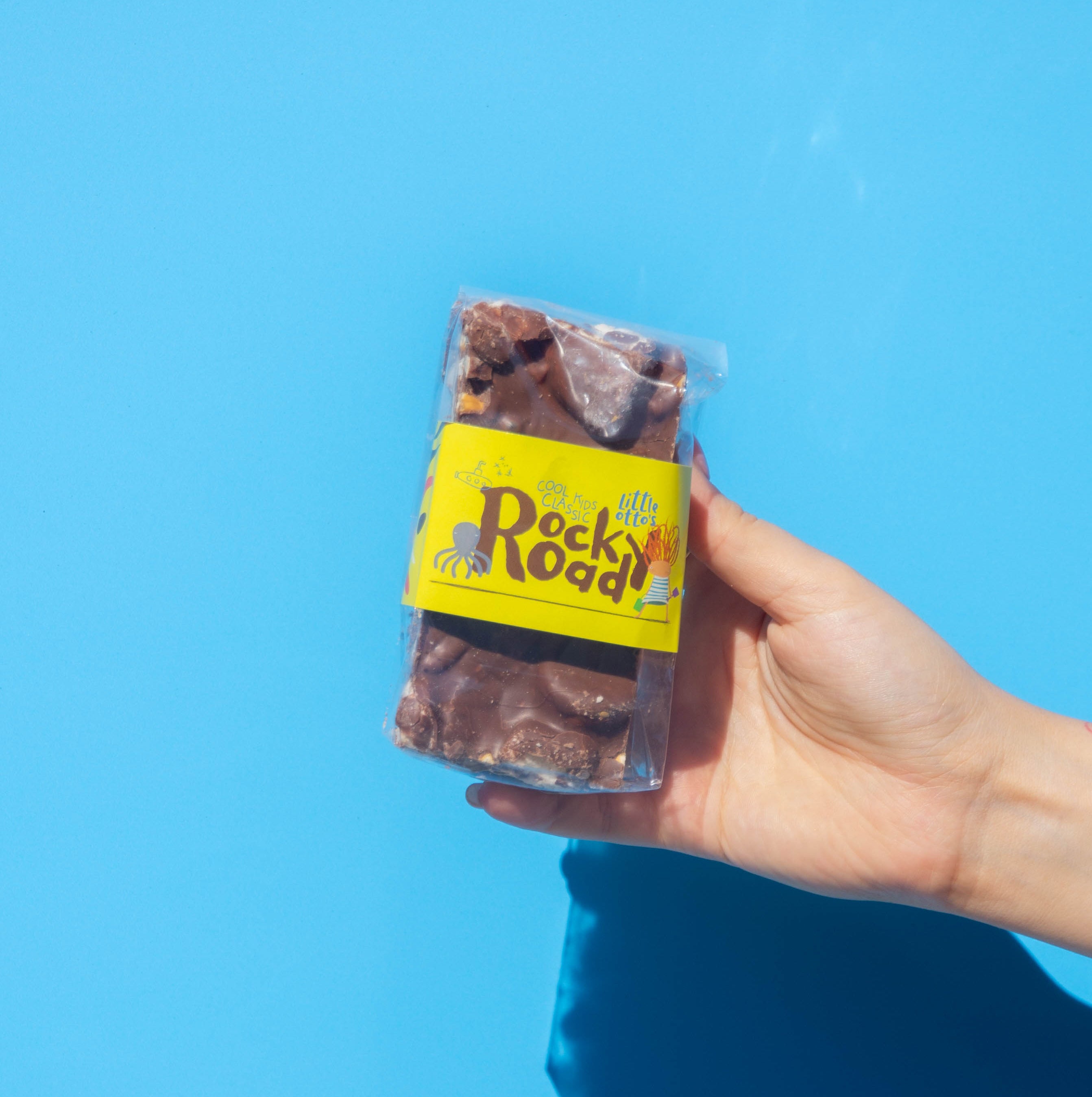 Little Otto's Staff holding Rocky Road cool kids classic 250g infront of Busselton blue wall