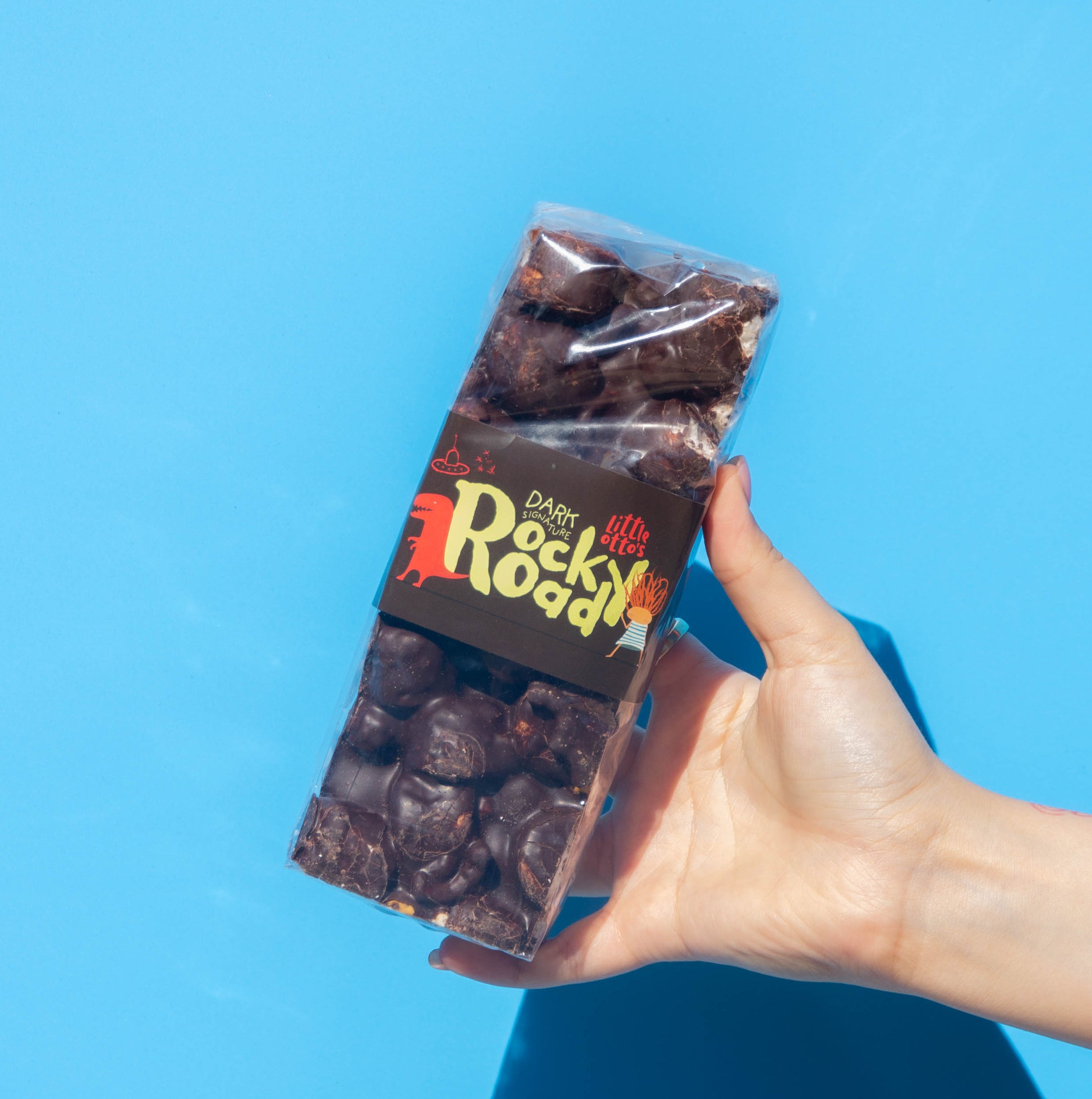 Little Otto's Staff holding Dark Chocolate Signature Rocky Road 500g infront of Busselton blue wall