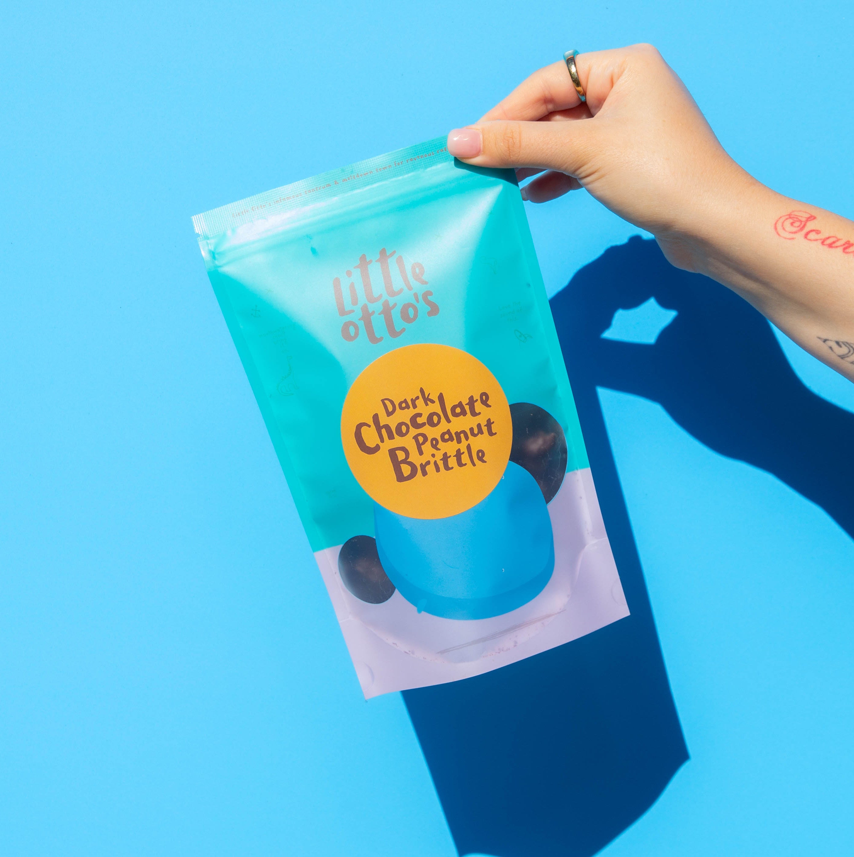 Little Otto's Staff holding dark choc peanut brittle infront of Busselton blue wall