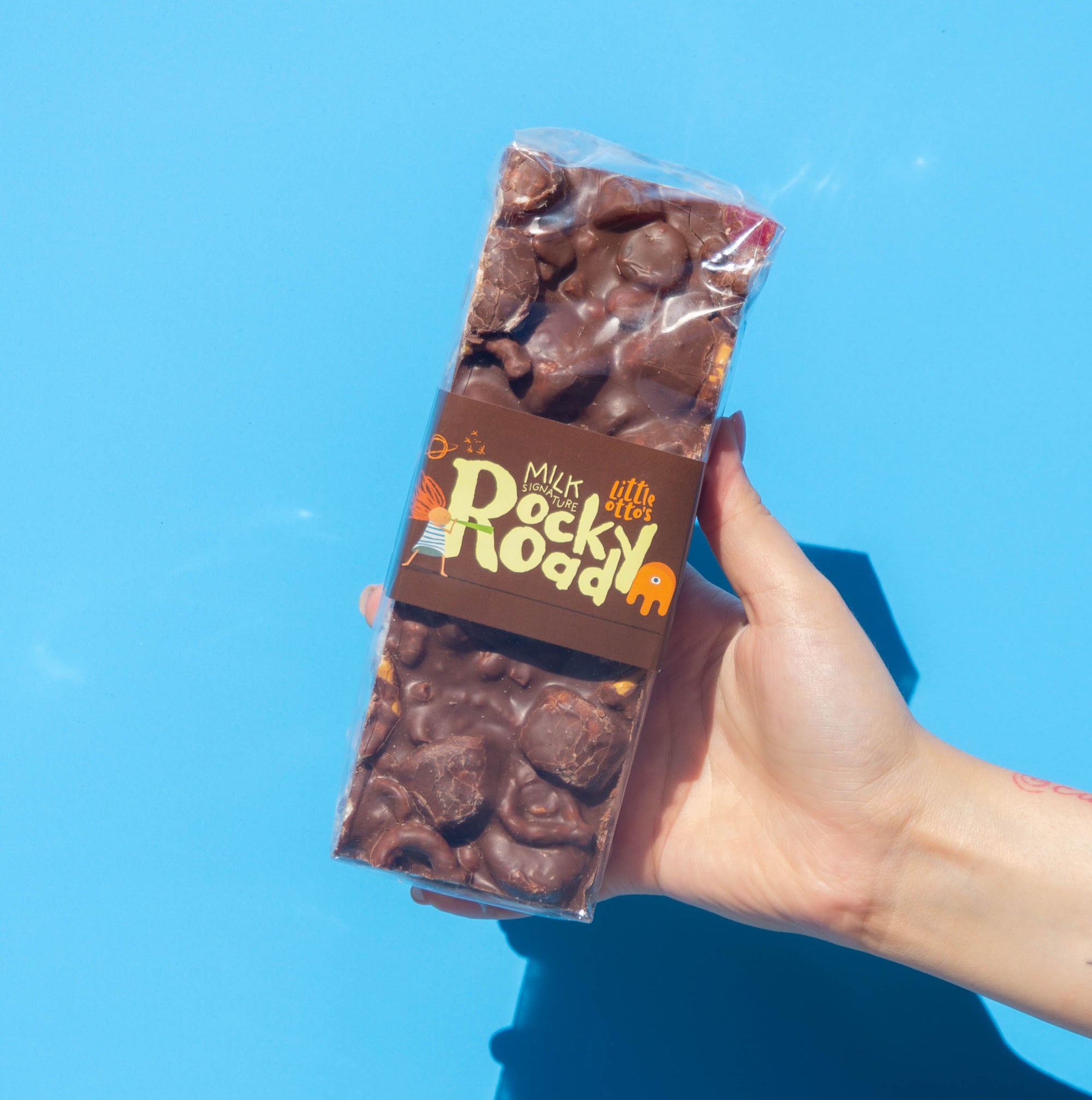 Little Otto's Staff holding milk choc signature rocky road 500 infront of Busselton blue wall